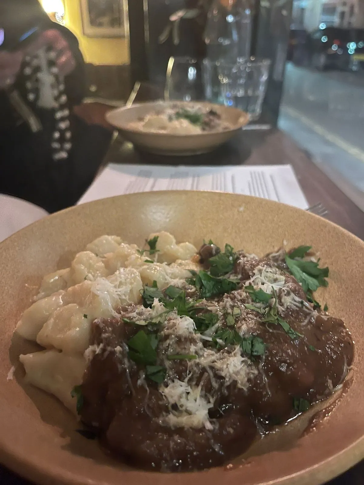 A bowl of gnocchi with venison pašticada, parsley and grated cheese