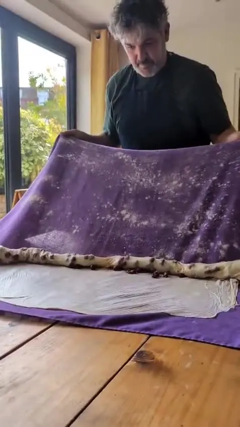Rolling a strudel inside a floured purple tablecloth