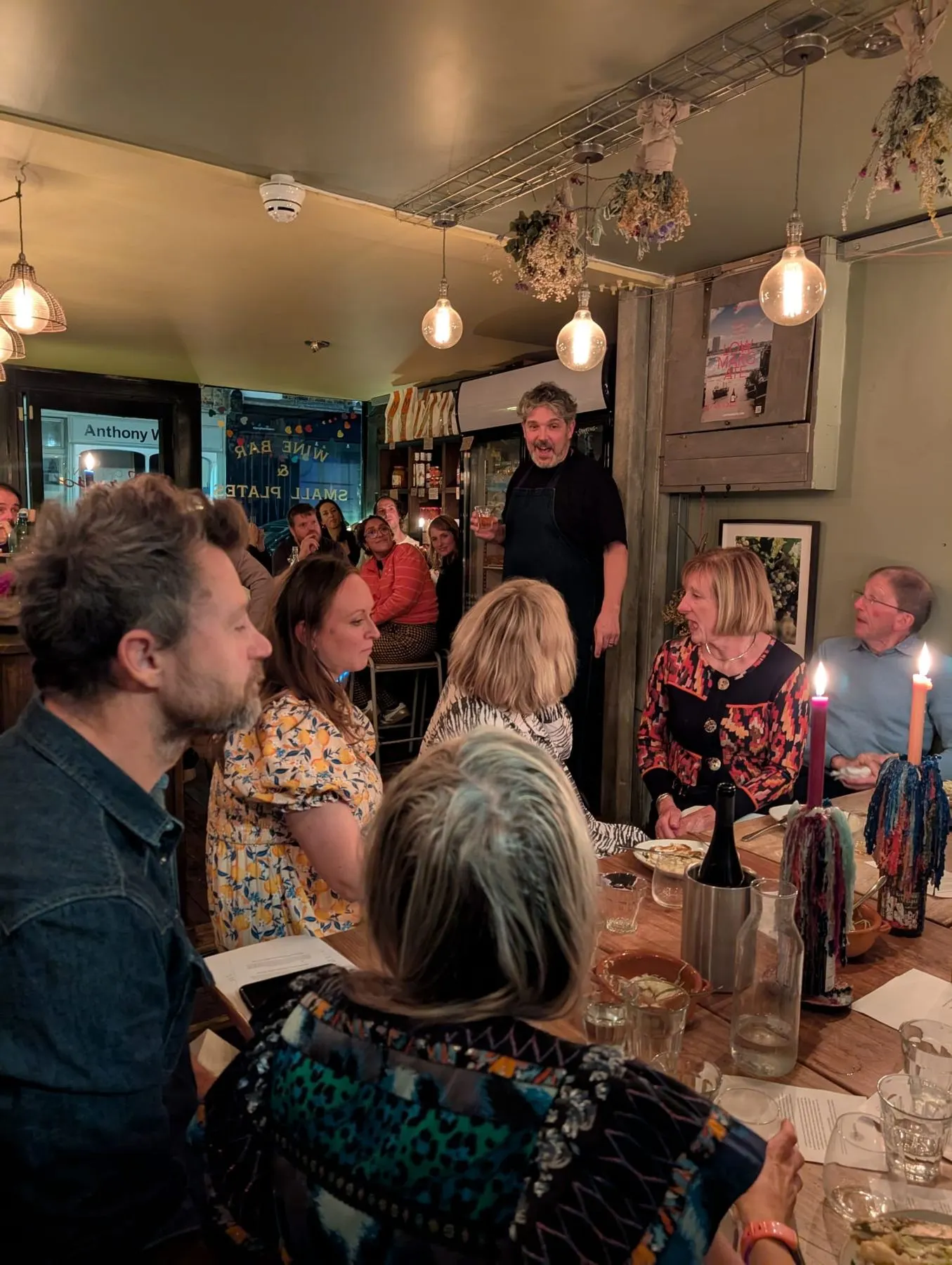 The host raising a glass to a full table inside the wine bar